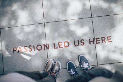 Two sets of feet with writing on a sidewalk that says passion led us here.