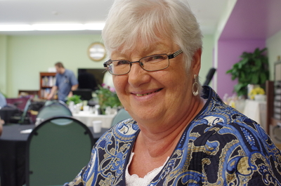 Smiling woman senior tenant with white hair and glasses in a community room.