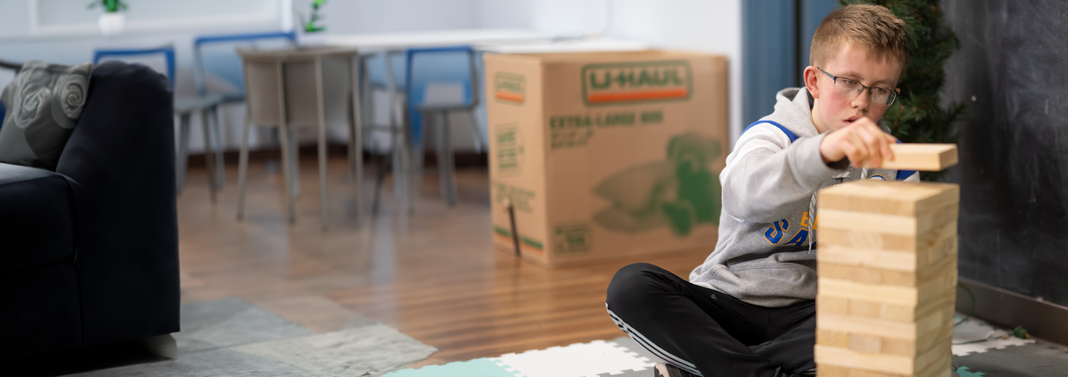 Young boy wearing glasses stacking Jenga blocks.