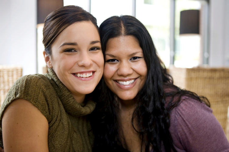 two women of mixed races smiling with heads together