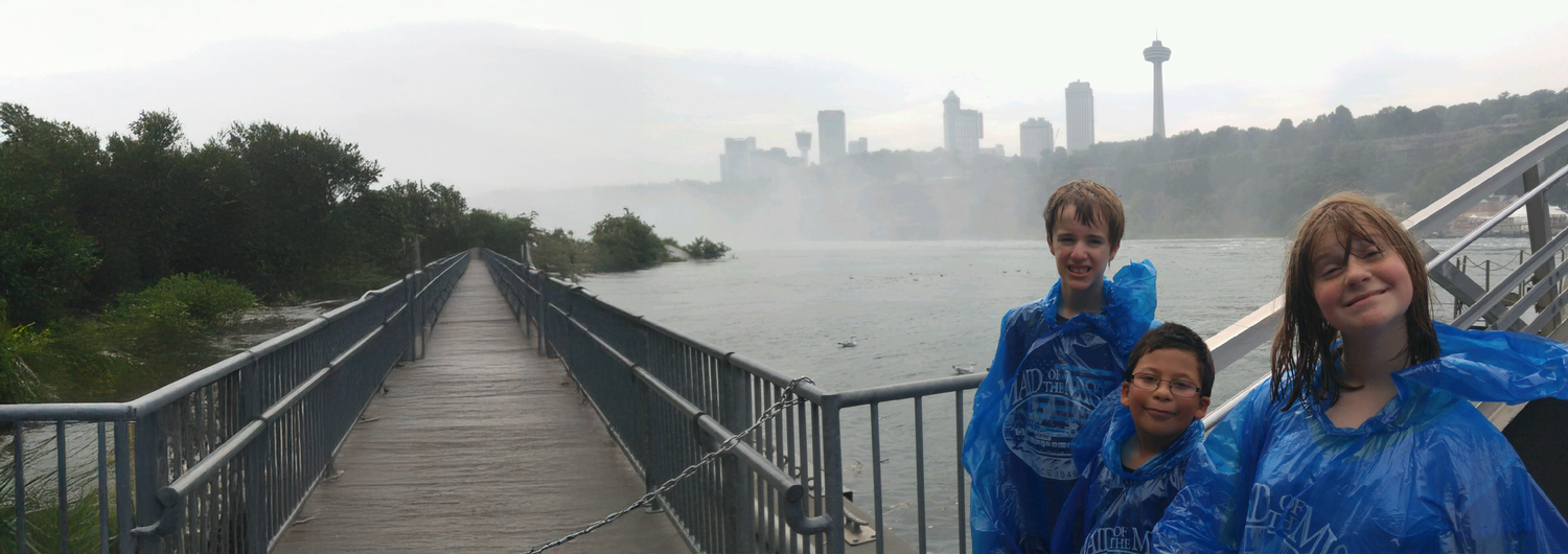 Group of smiling children wear rain ponchos at Niagara Falls New York, backed by the Canadian Niagara Falls skyline.