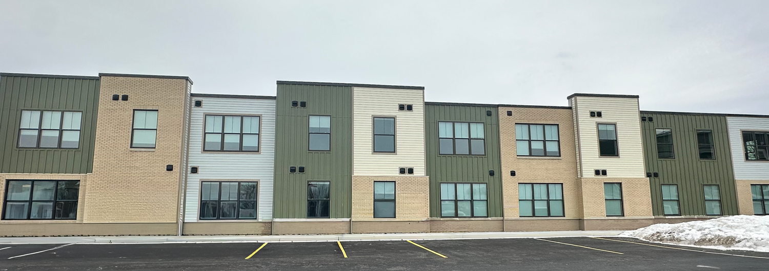 A construction image of a multi-unit apartment building, constructed of red brick, white and olive green siding.