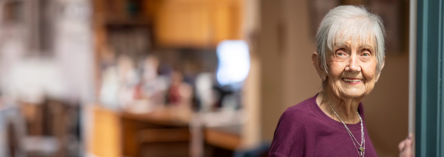 Senior woman smiling standing in an apartment doorframe.