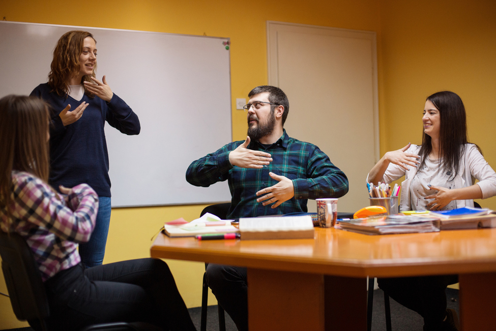 Three adults in a meeting room communicating with ASL