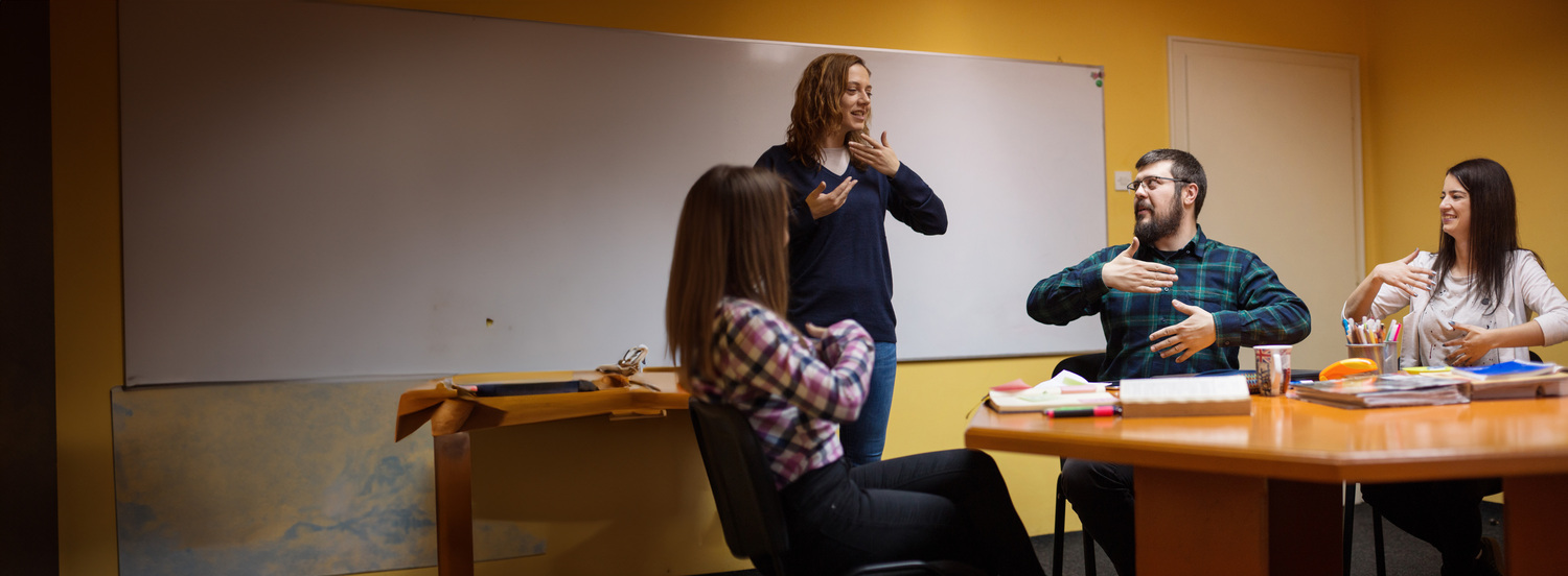 Three adults in a meeting room communicating with ASL