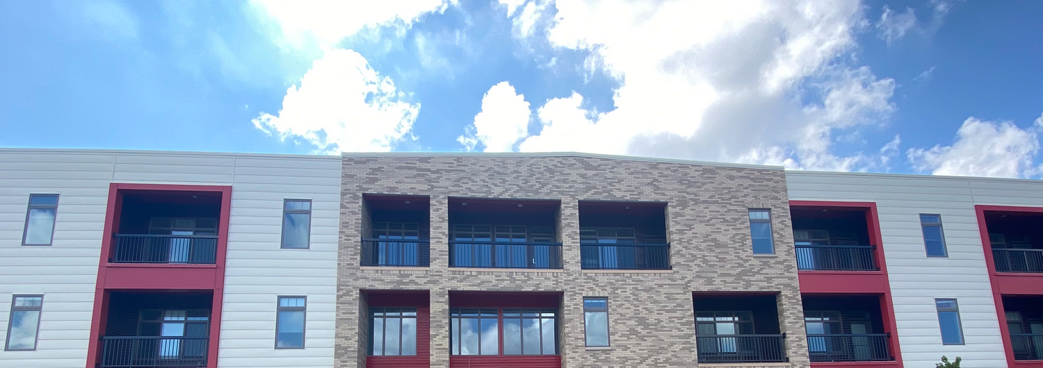 Top of apartment building with a blue, cloud dotted sky.