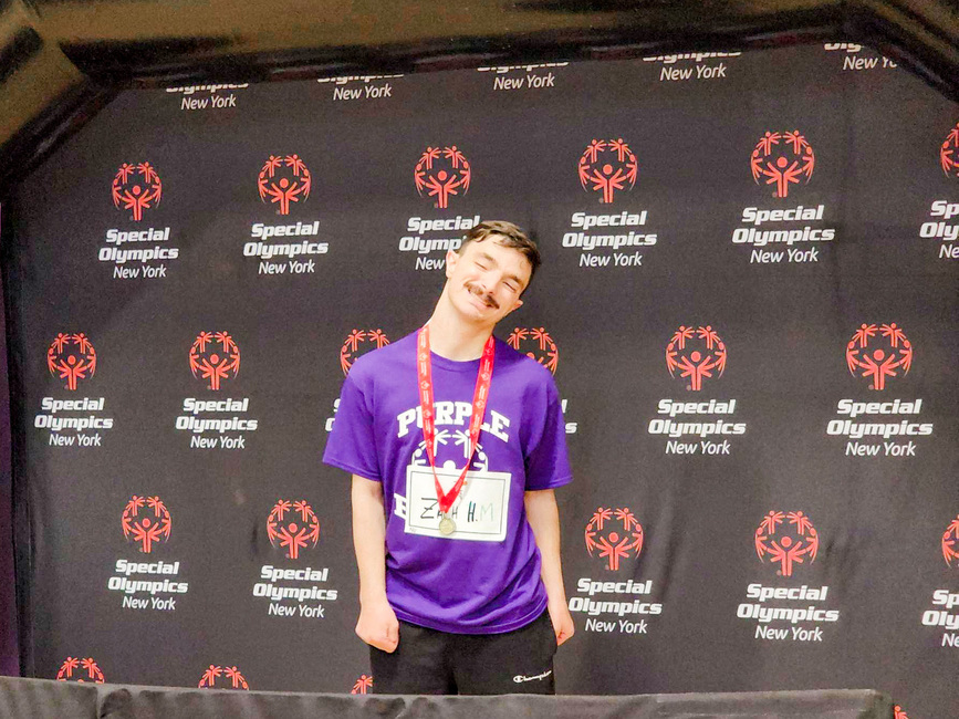 Medal Winner Grinning in front of Special Olympics Logo
